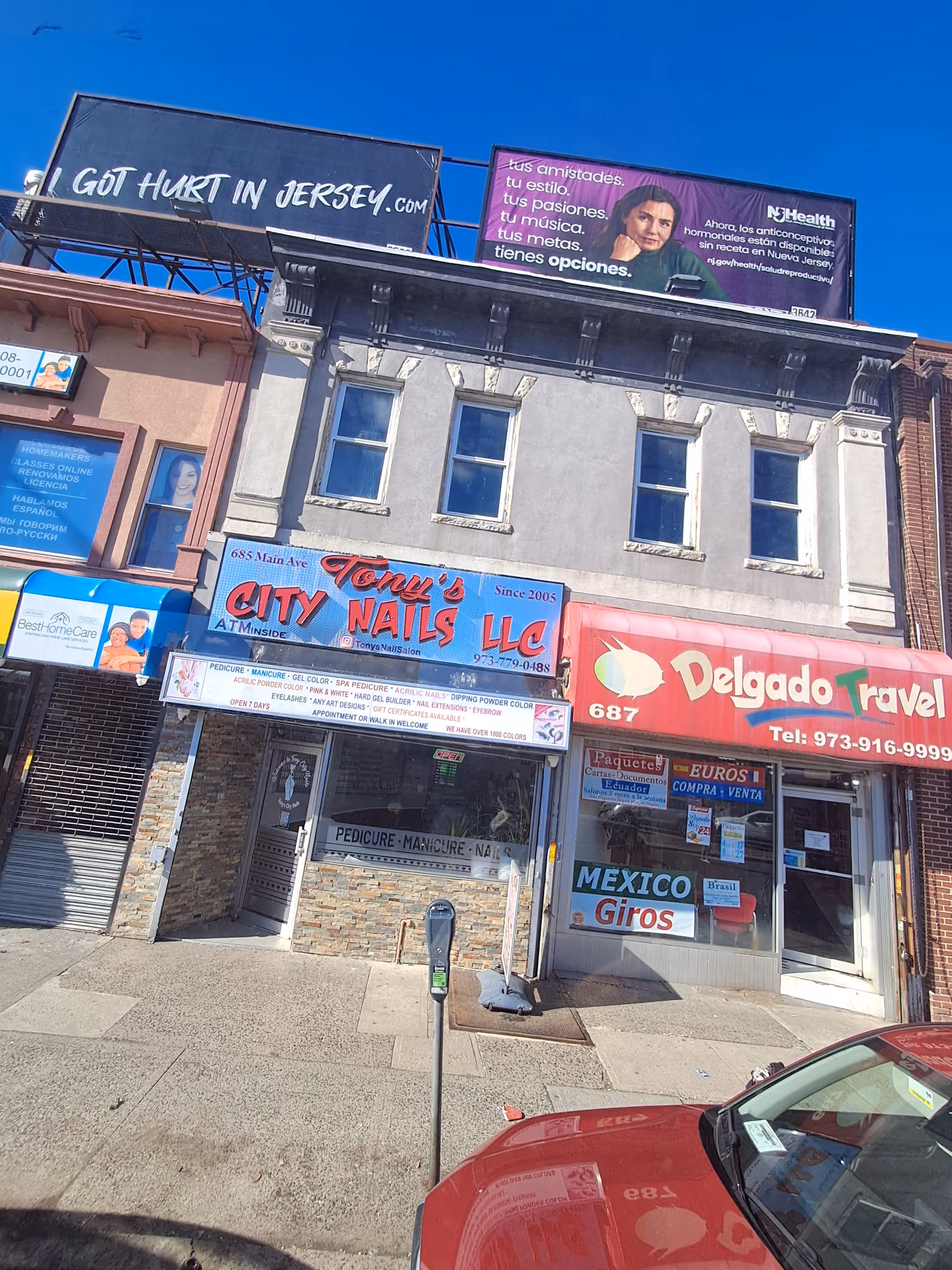 Busy storefront row with multiple signs including Tony's Nails and Delgado Travel on a city street.