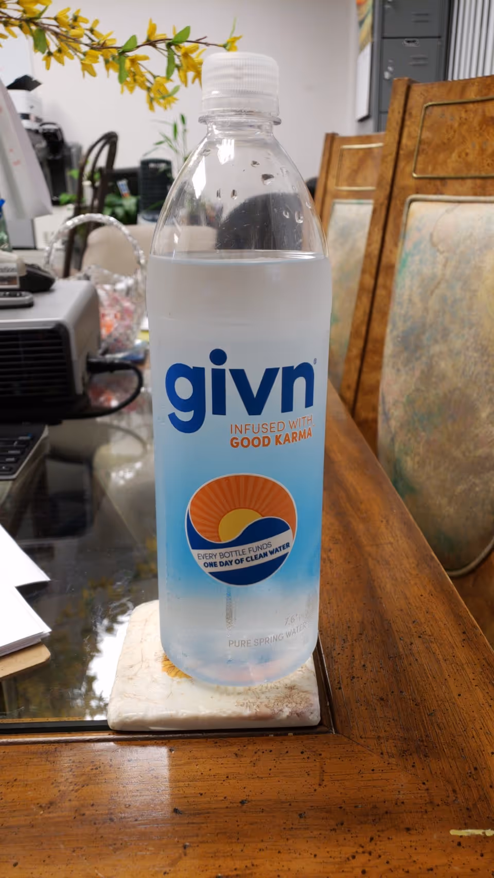 A plastic water bottle labeled givn sits on a wooden desk in an office.