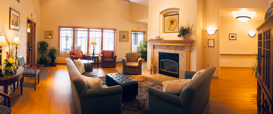 Cozy senior living lounge with sofas, chairs, a fireplace, and warm lighting.