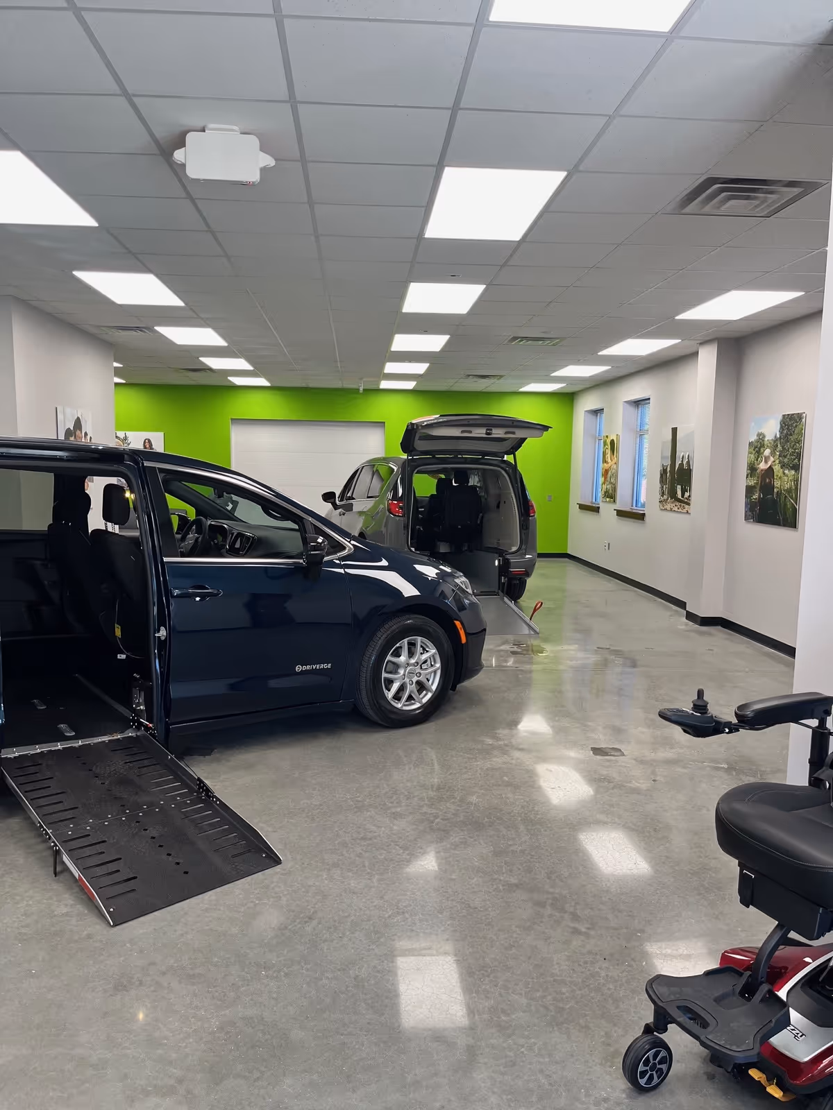 Indoor showroom with wheelchair-accessible vans, a ramp, and a mobility scooter in view.