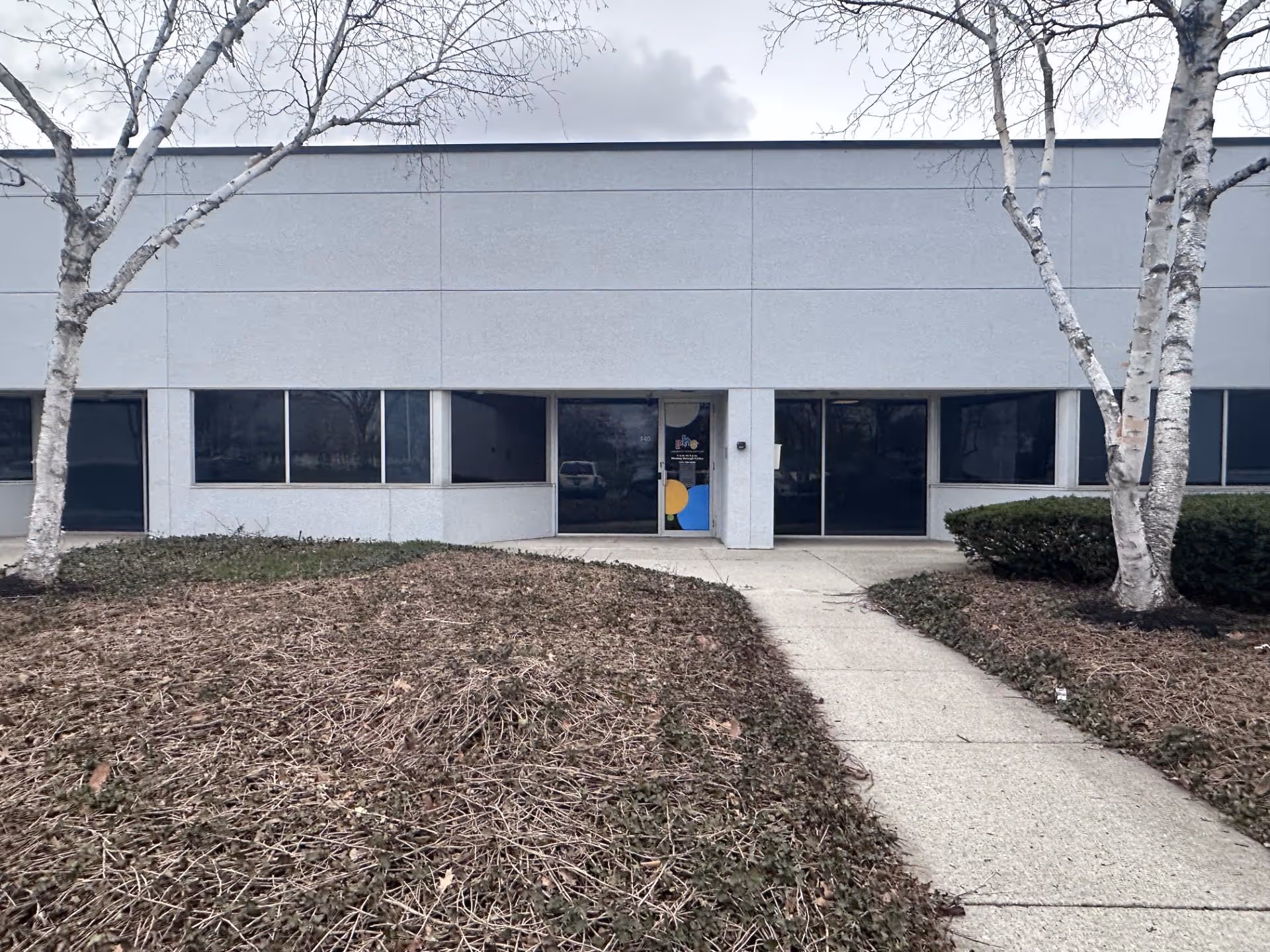 Front exterior of a gray building with glass doors and a sidewalk path.