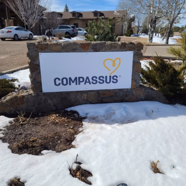 Stone sign reading Compassus in front of building with snow on the ground.
