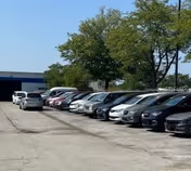Line of parked cars along a curb with a blue building and trees in the background.