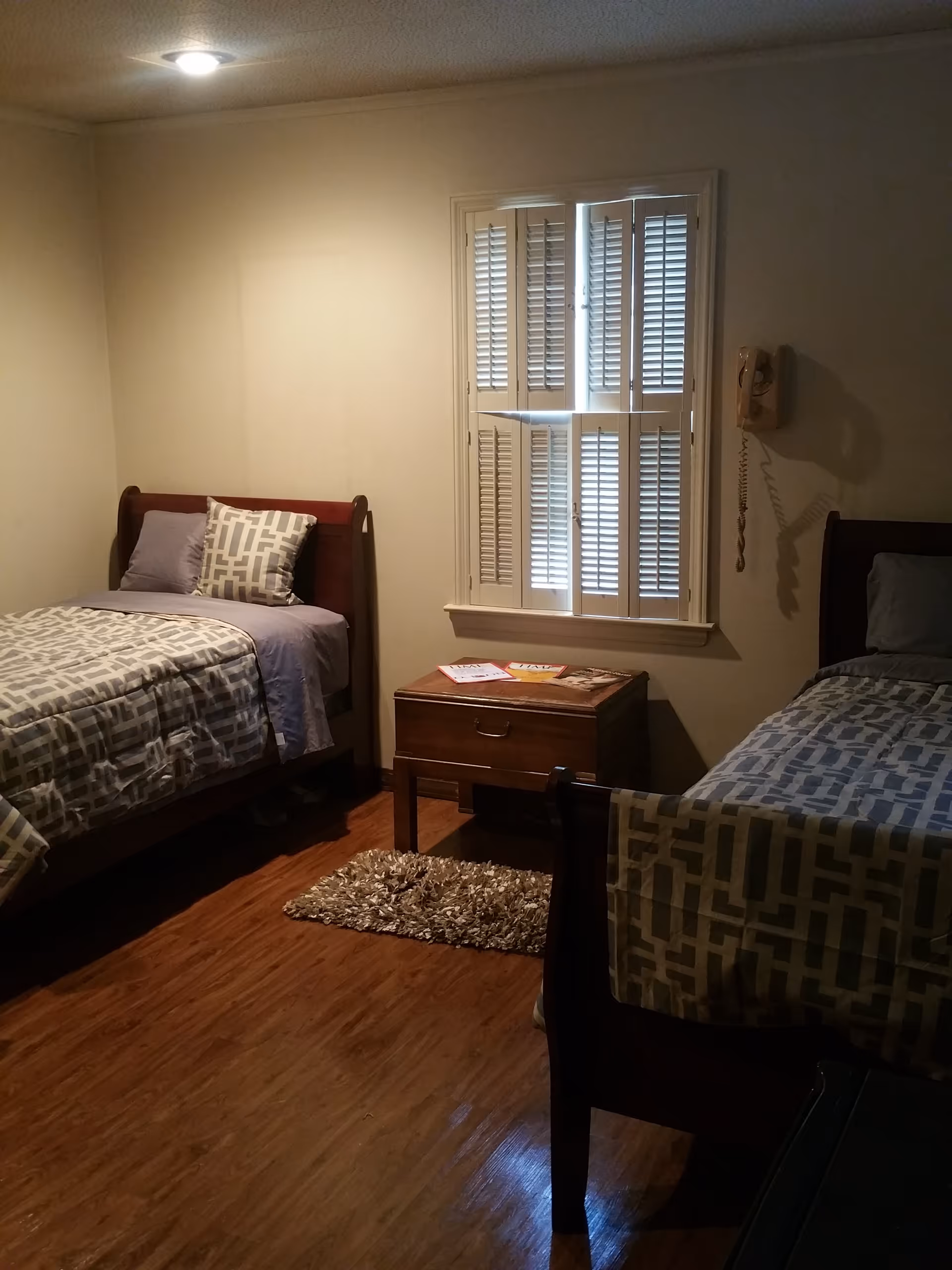 Two twin beds with matching geometric quilts, a nightstand between, and a window with shutters