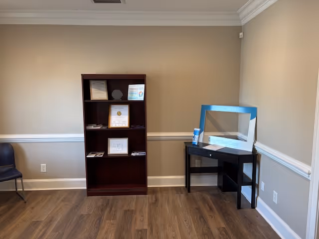 Interior reception area with dark wood bookshelf, small desk with blue frame, chair.