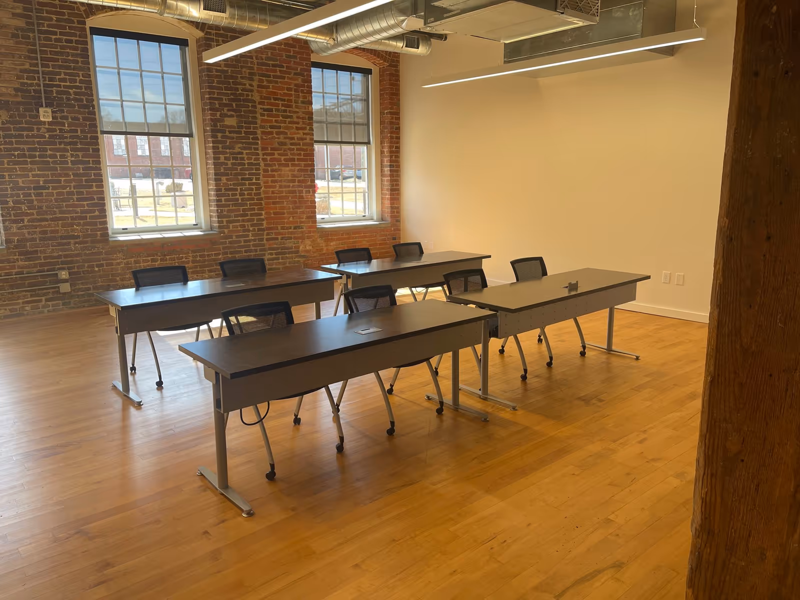 Interior training room with brick walls, large windows, exposed ducts, and rows of long desks.