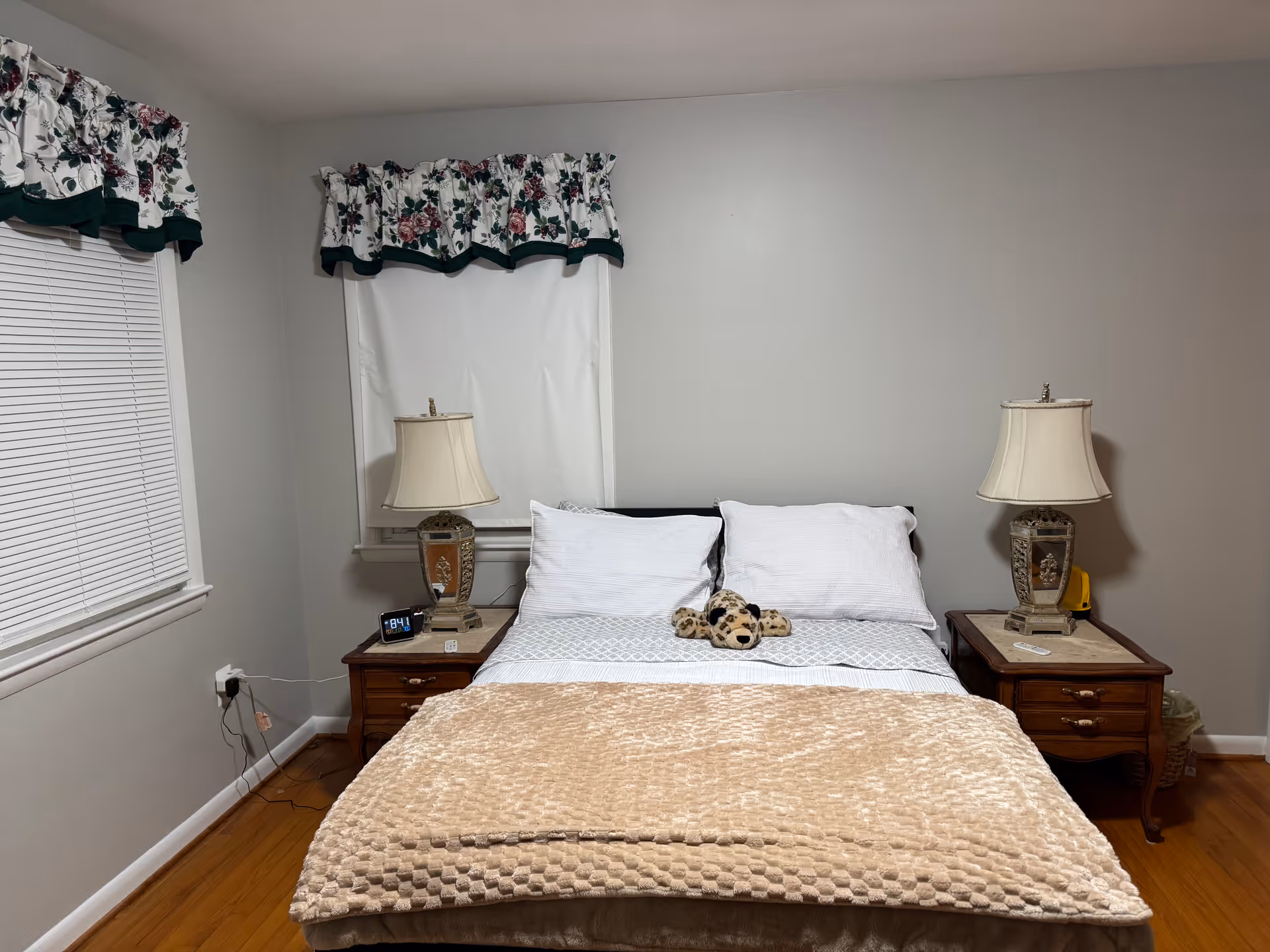 Bedroom scene with a bed, two nightstands, lamps, and a stuffed teddy on the blanket.