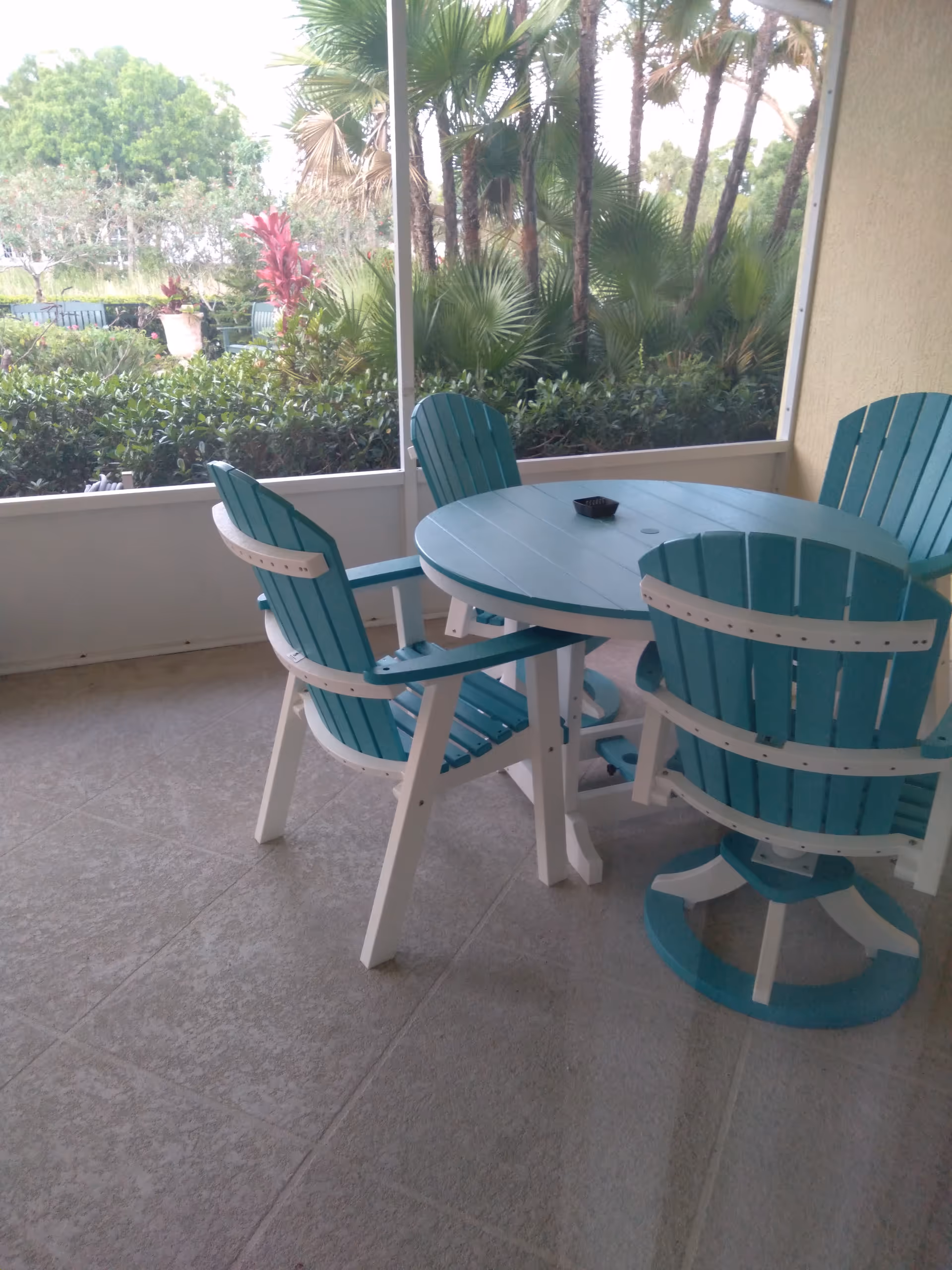 Outdoor screened patio with turquoise Adirondack chairs around a round table.