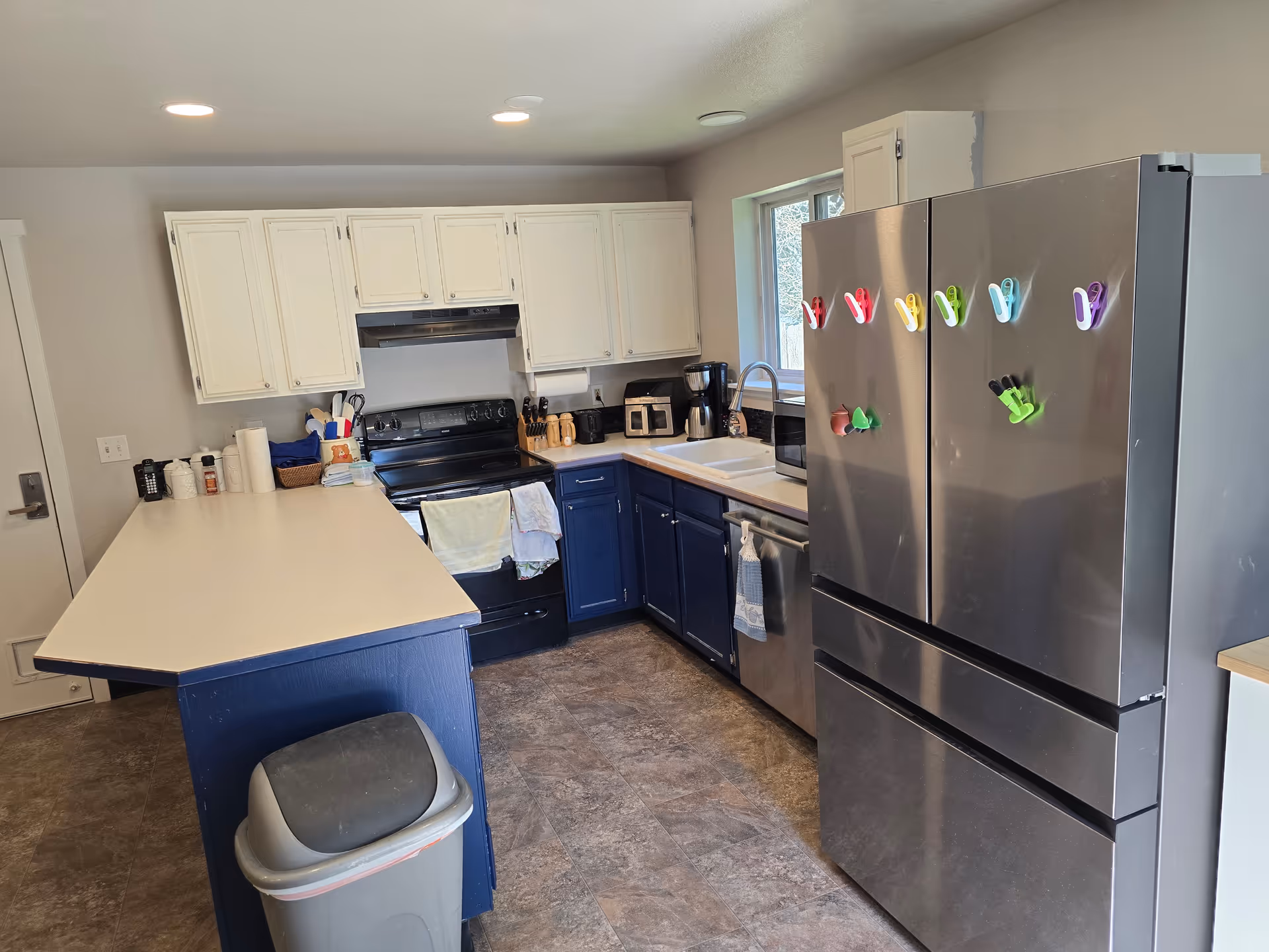 Spacious kitchen with white upper cabinets, blue lower cabinets, and a stainless fridge.