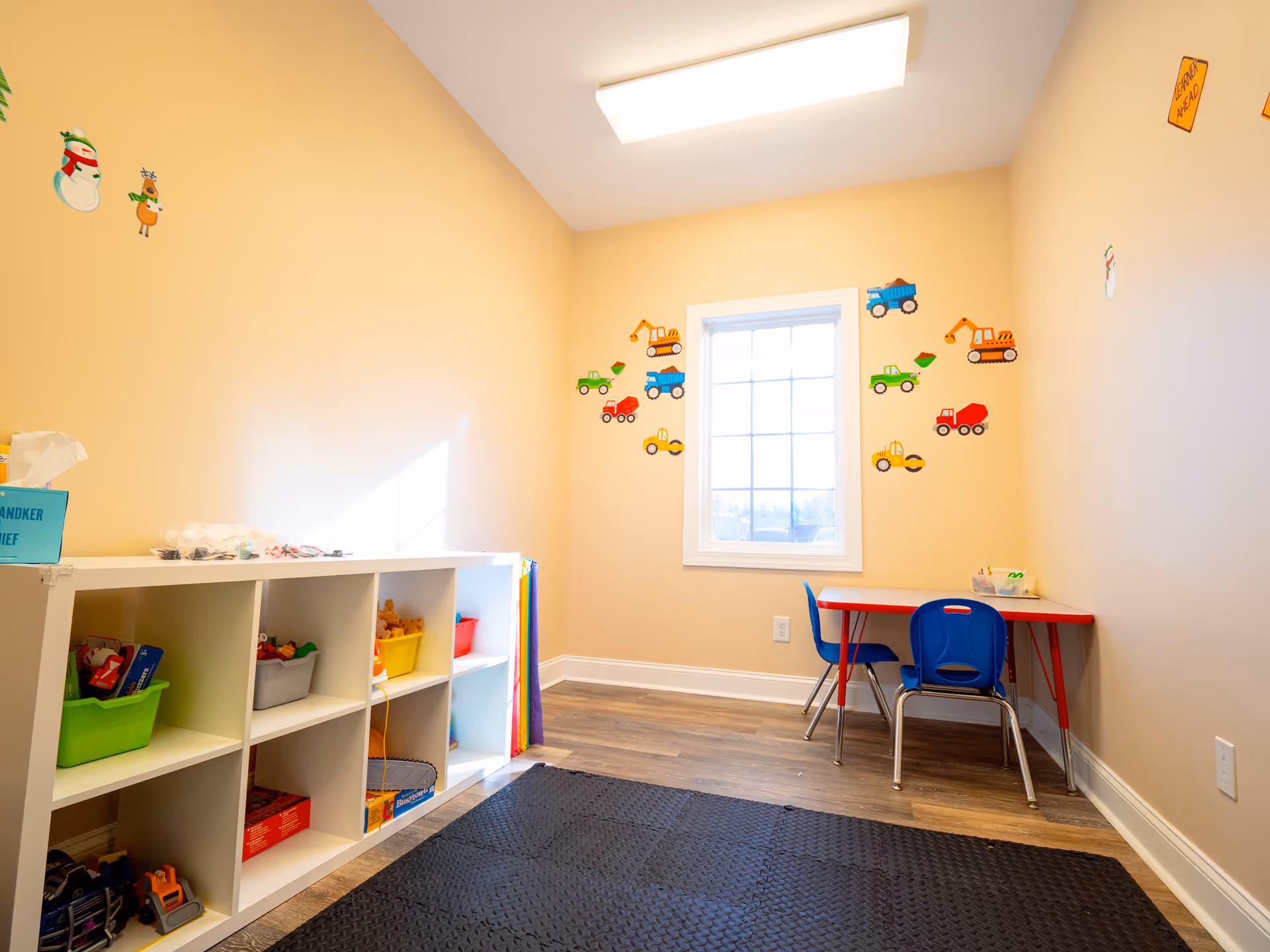 A small children's play area with cubbies, toy bins, a red table, and blue chairs.