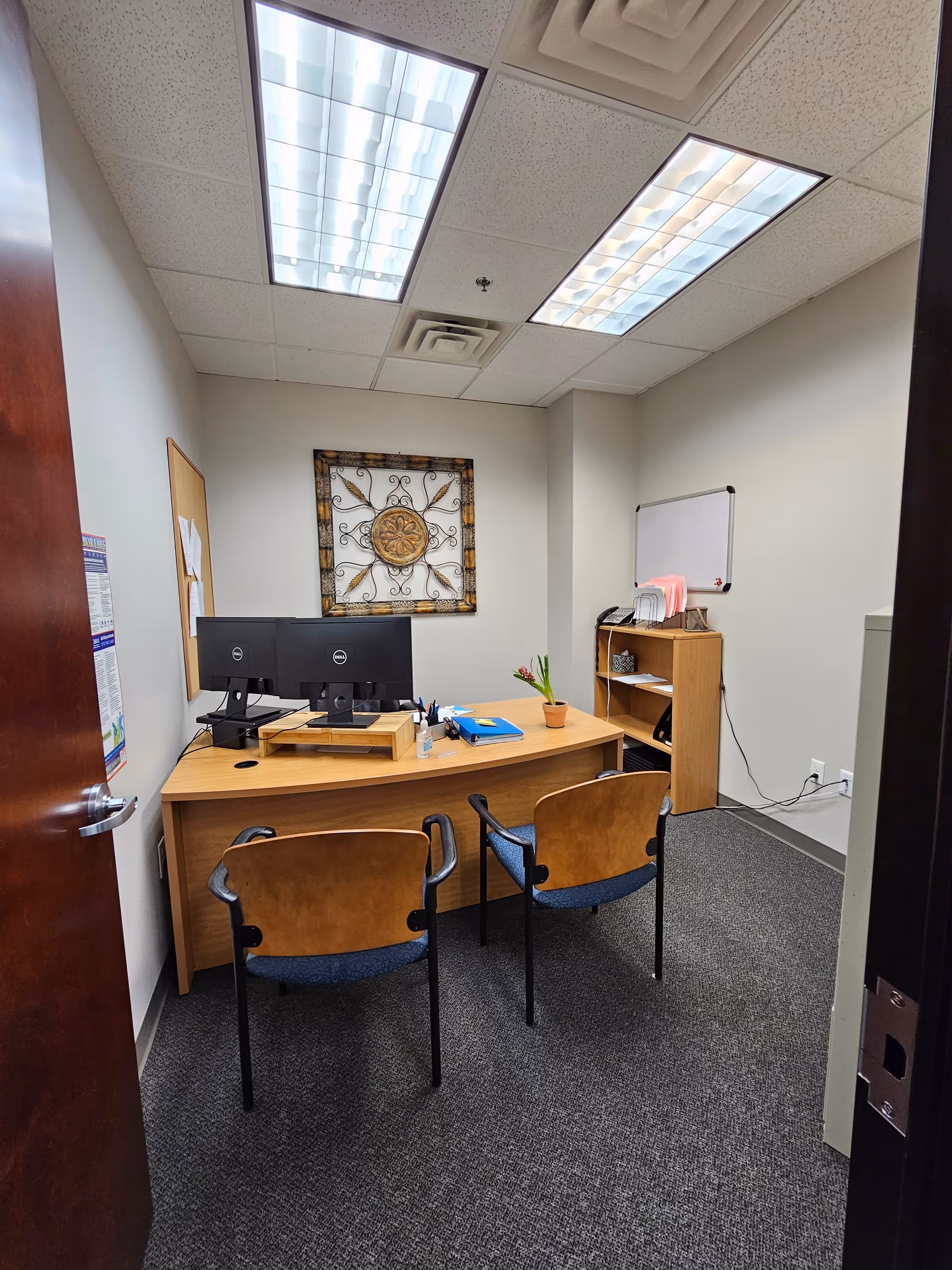 Small office in a senior facility with desk, dual monitors, chairs, and a whiteboard.
