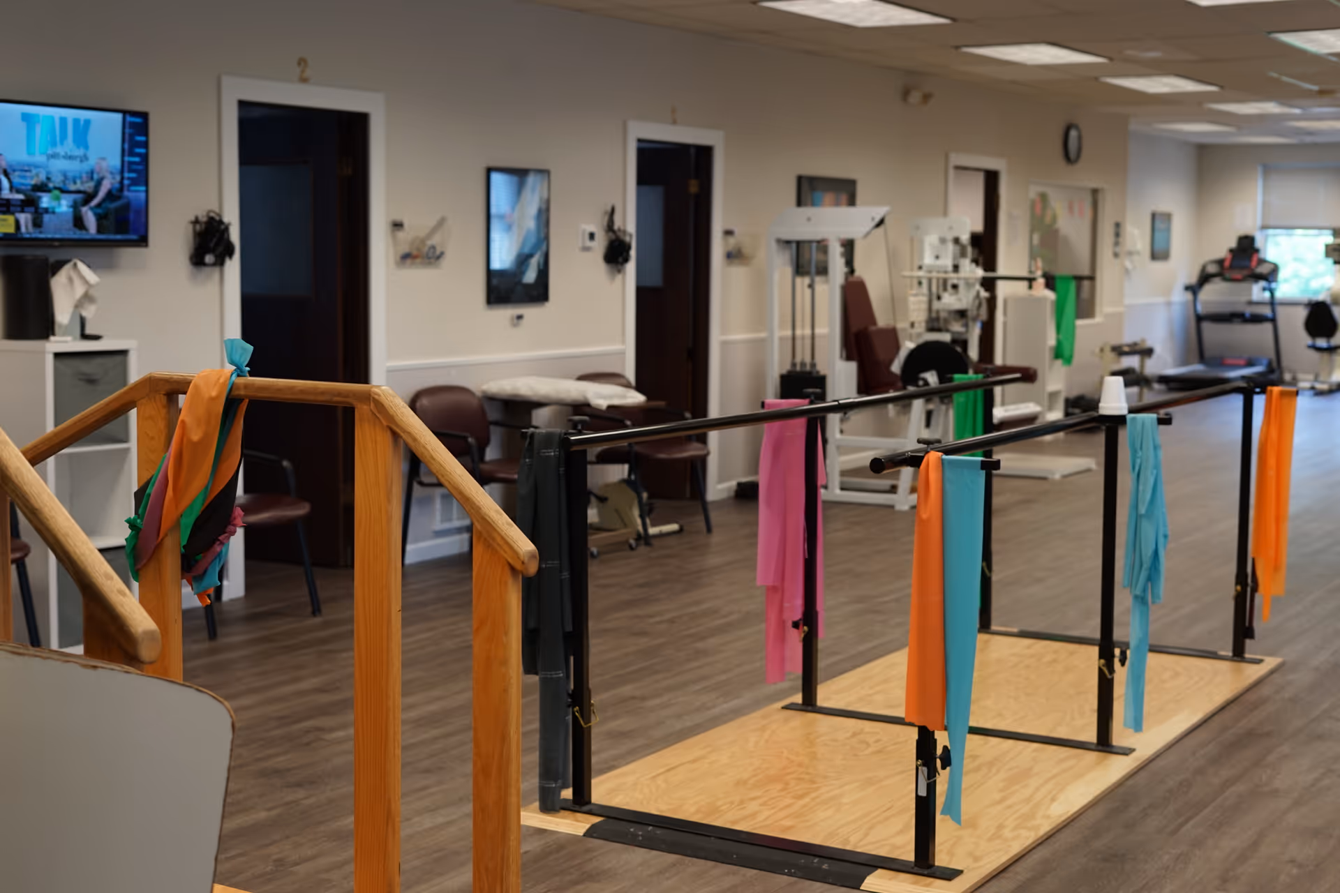 Indoor physical therapy gym with parallel bars, colorful towels, and rehabilitation equipment.