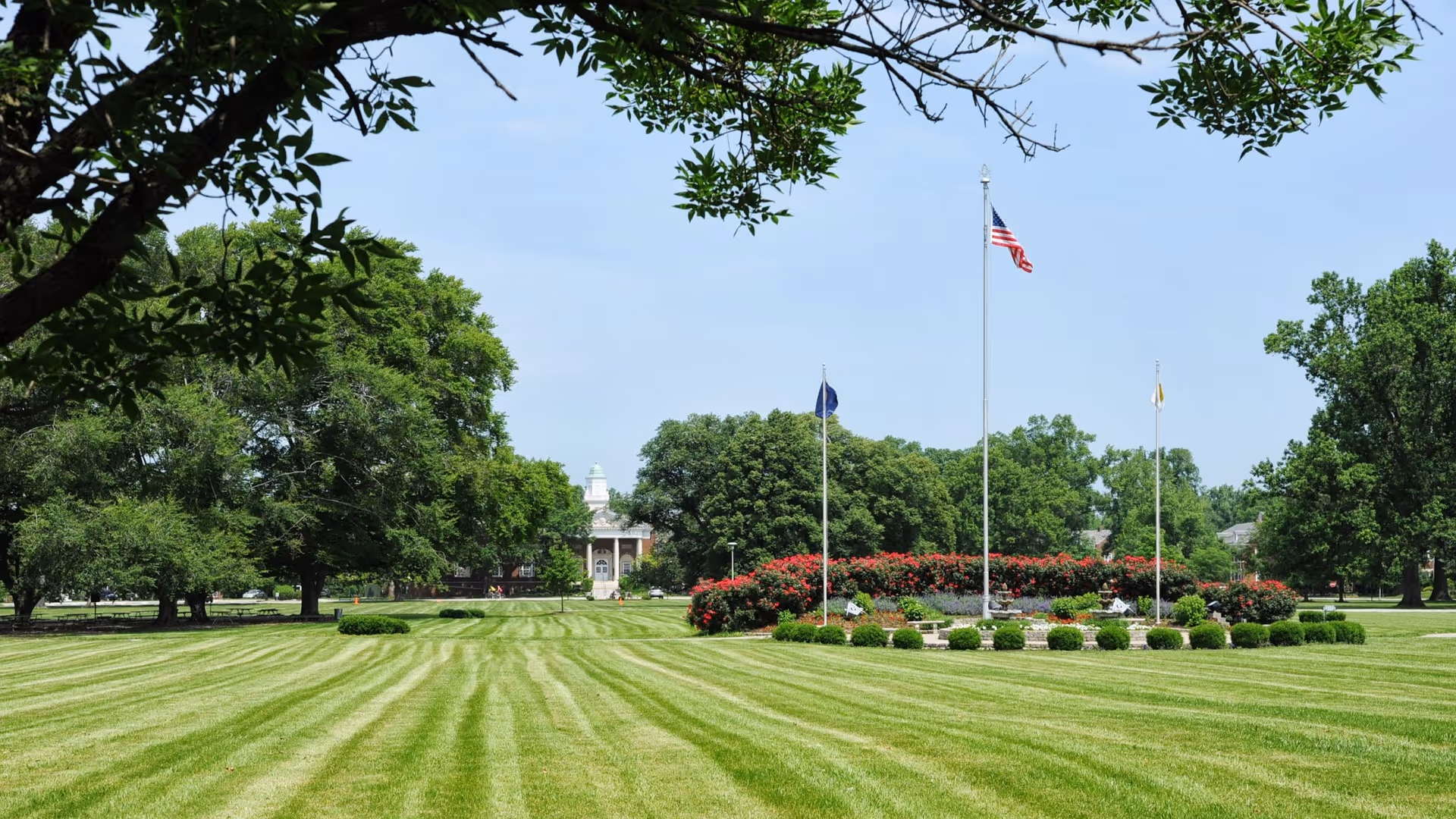 A well-manicured lawn with flagpoles, shrubs, and distant buildings at Masonic Homes Kentucky.