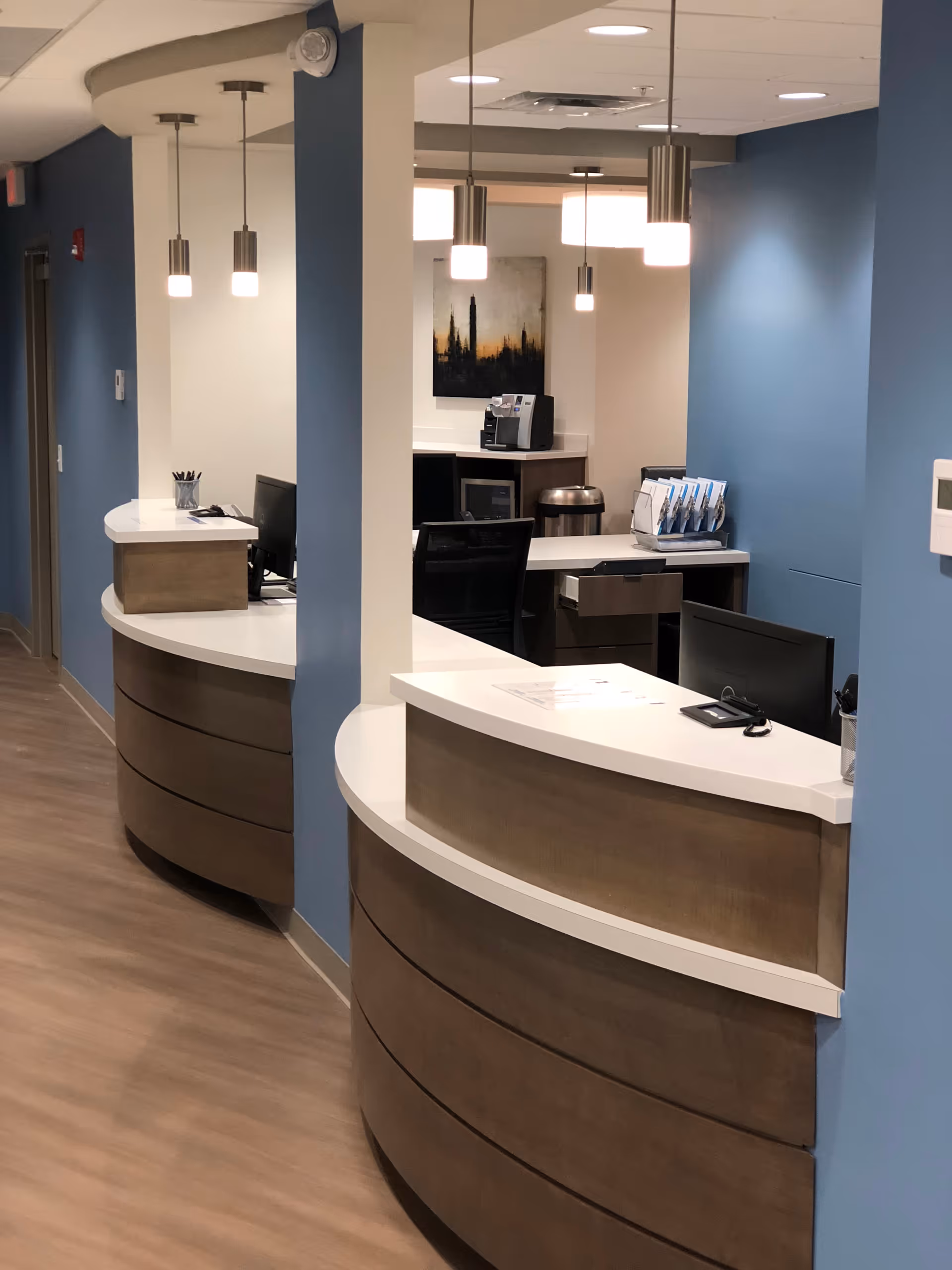 Curved reception desks with white countertops and wood panels in a blue-walled lobby.