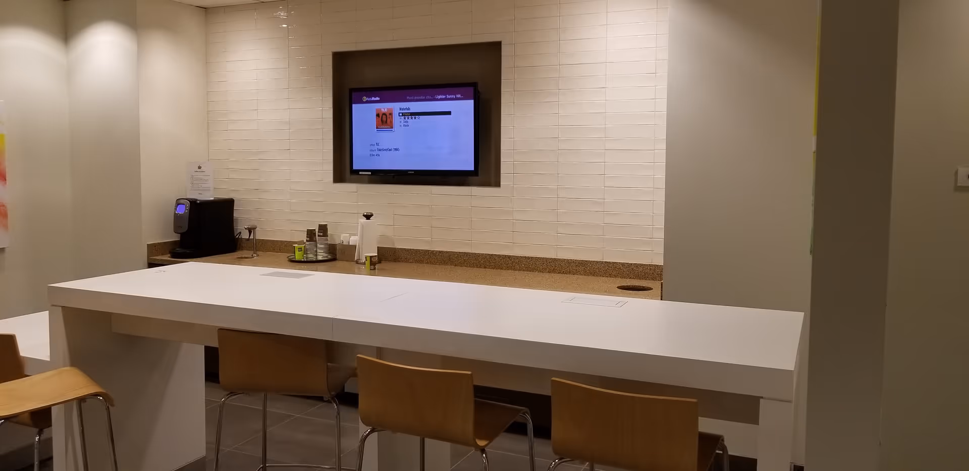 Modern reception area with a white high counter, stools, and a wall-mounted monitor.