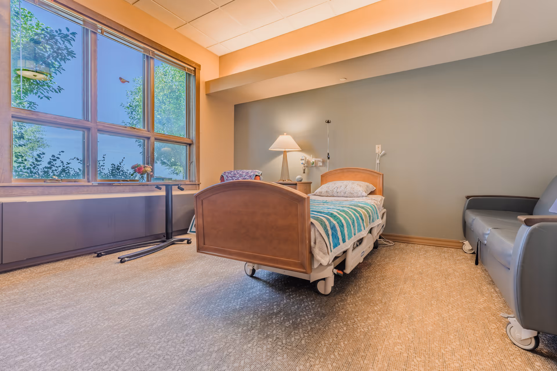 Hospice patient bedroom with a single bed, window view, and lounge chair.