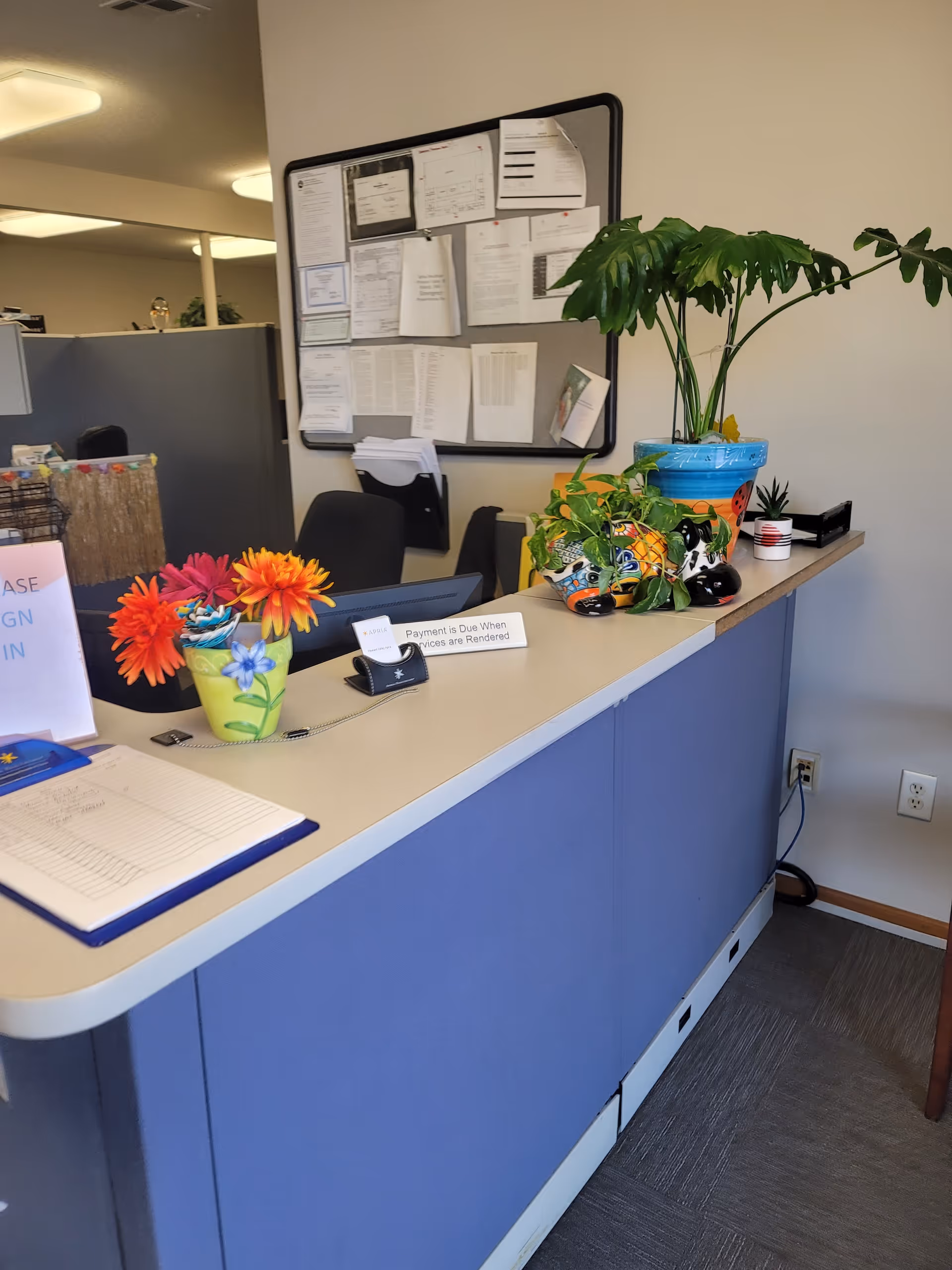 Reception desk with blue front panels, plants, and a notice board in a senior living facility.