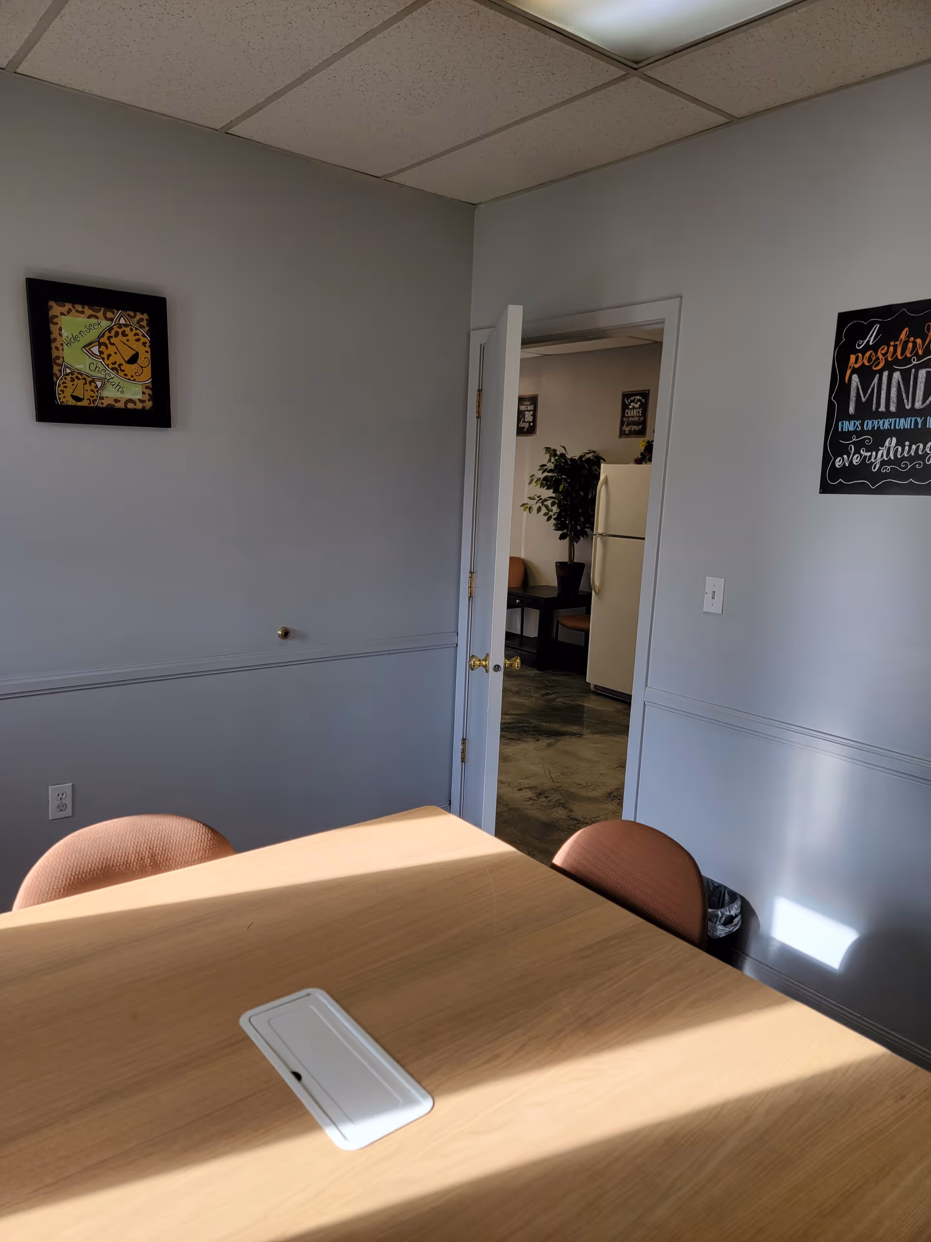 Light-filled dining room with wooden table, pinkish chairs, and doorway to kitchen.