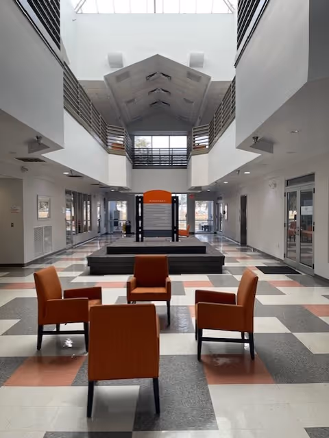 Bright spacious lobby with orange chairs around a central information display in a modern facility.