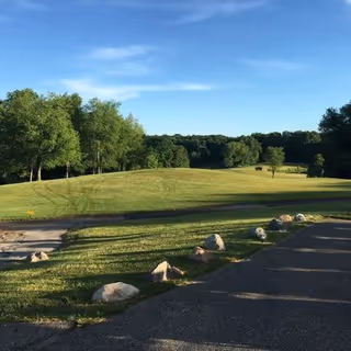 Sunlit lawn with trees and a paved path bordered by rocks under a blue sky