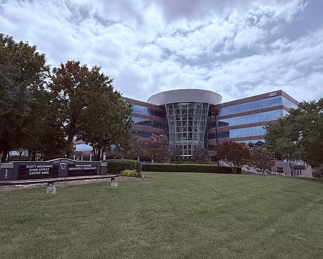 Exterior view of a modern glass-front building with a circular atrium and lawn.