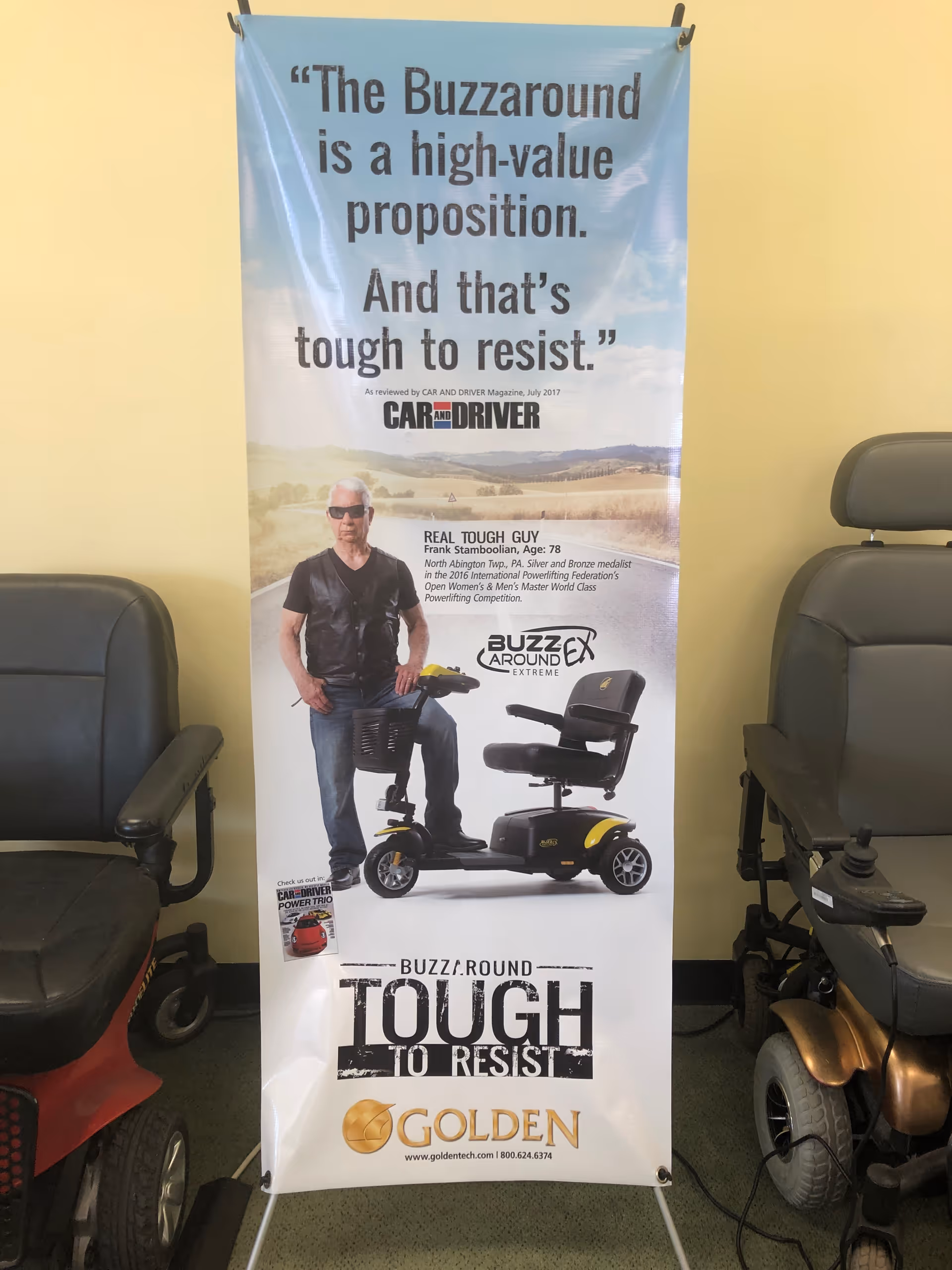 Indoor showroom with a tall Buzzaround banner and mobility scooters on display.