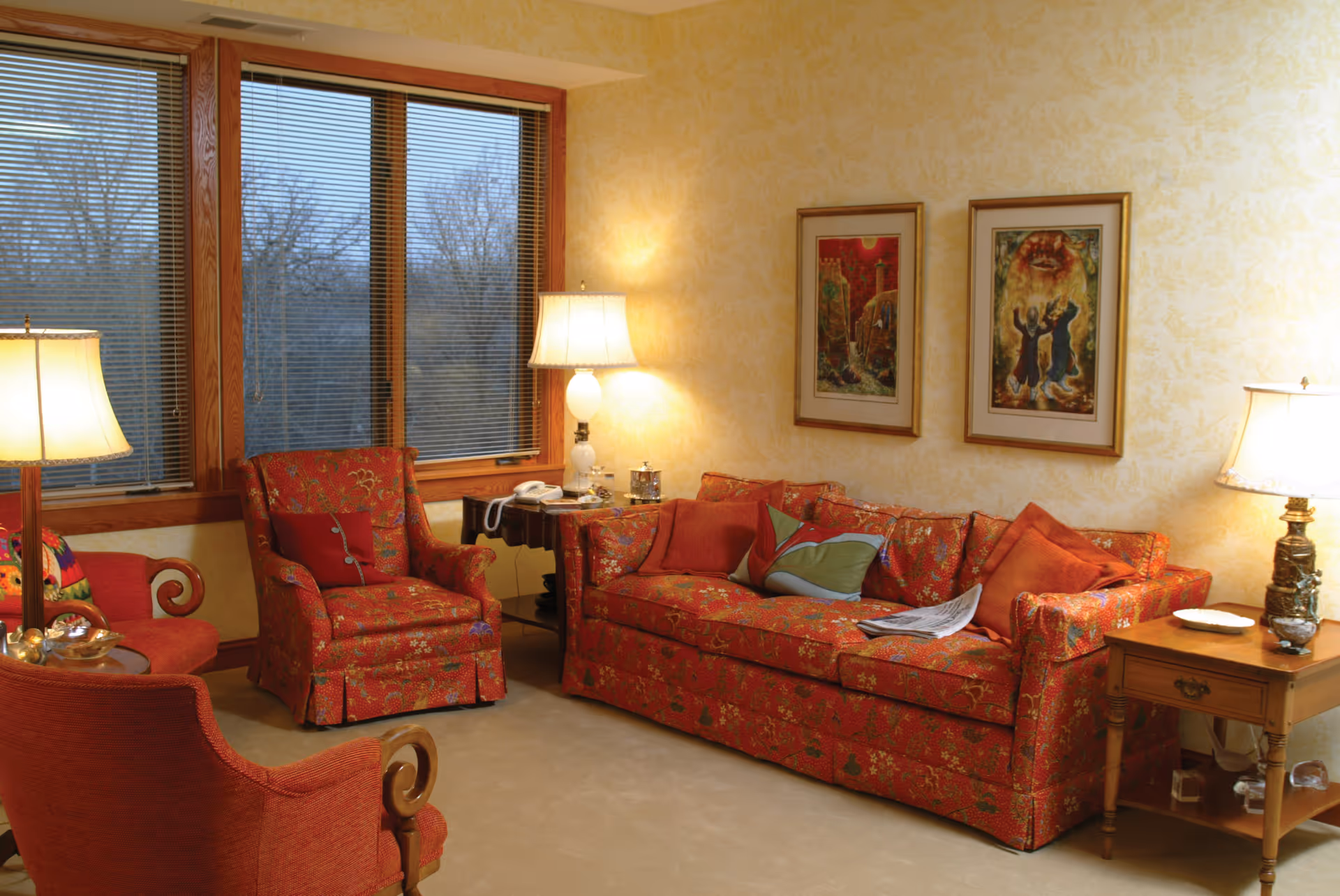 Cozy living room with red patterned sofa and armchairs, lamps, and wall art.