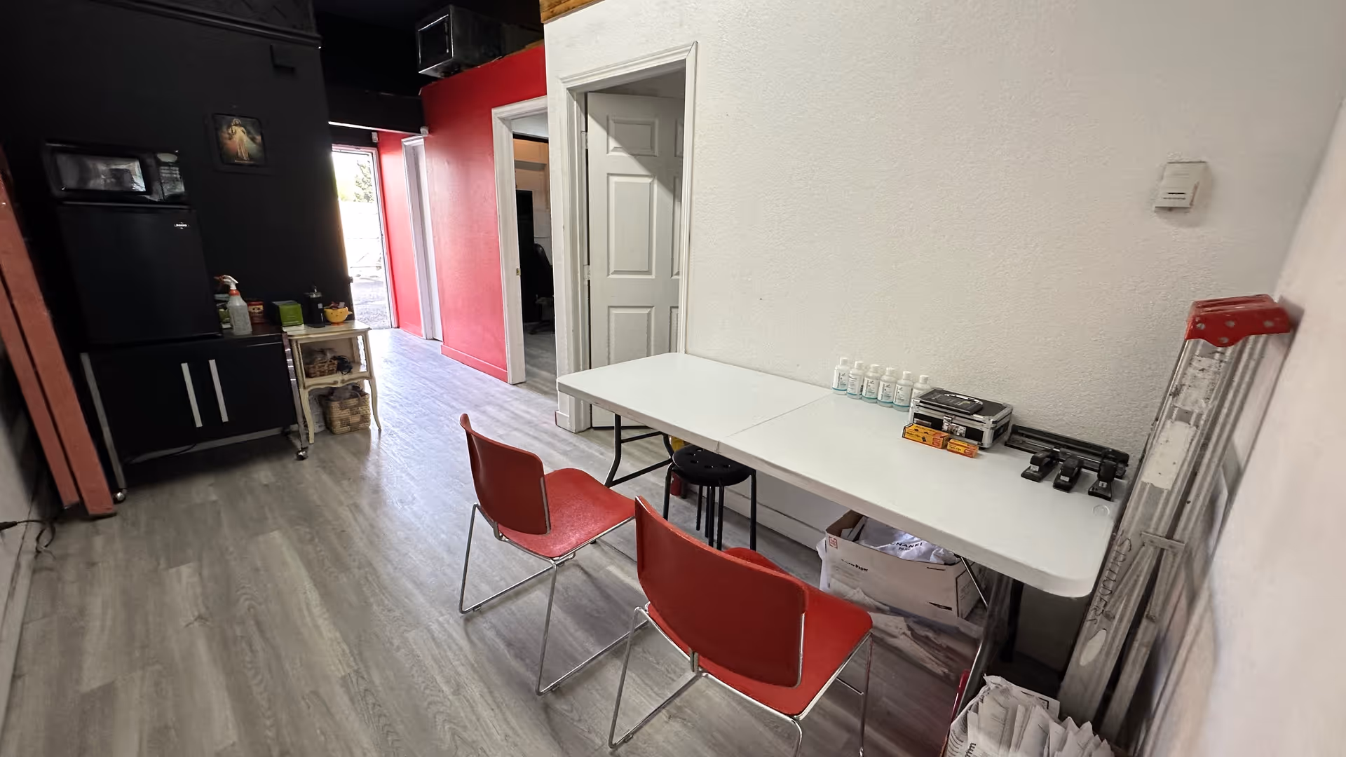 Utility room with long table, red chairs, and cleaning supplies along walls.