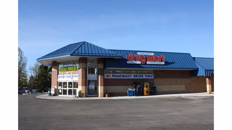 Blue-roofed Discount Drug Mart storefront with a pharmacy drive-thru sign.