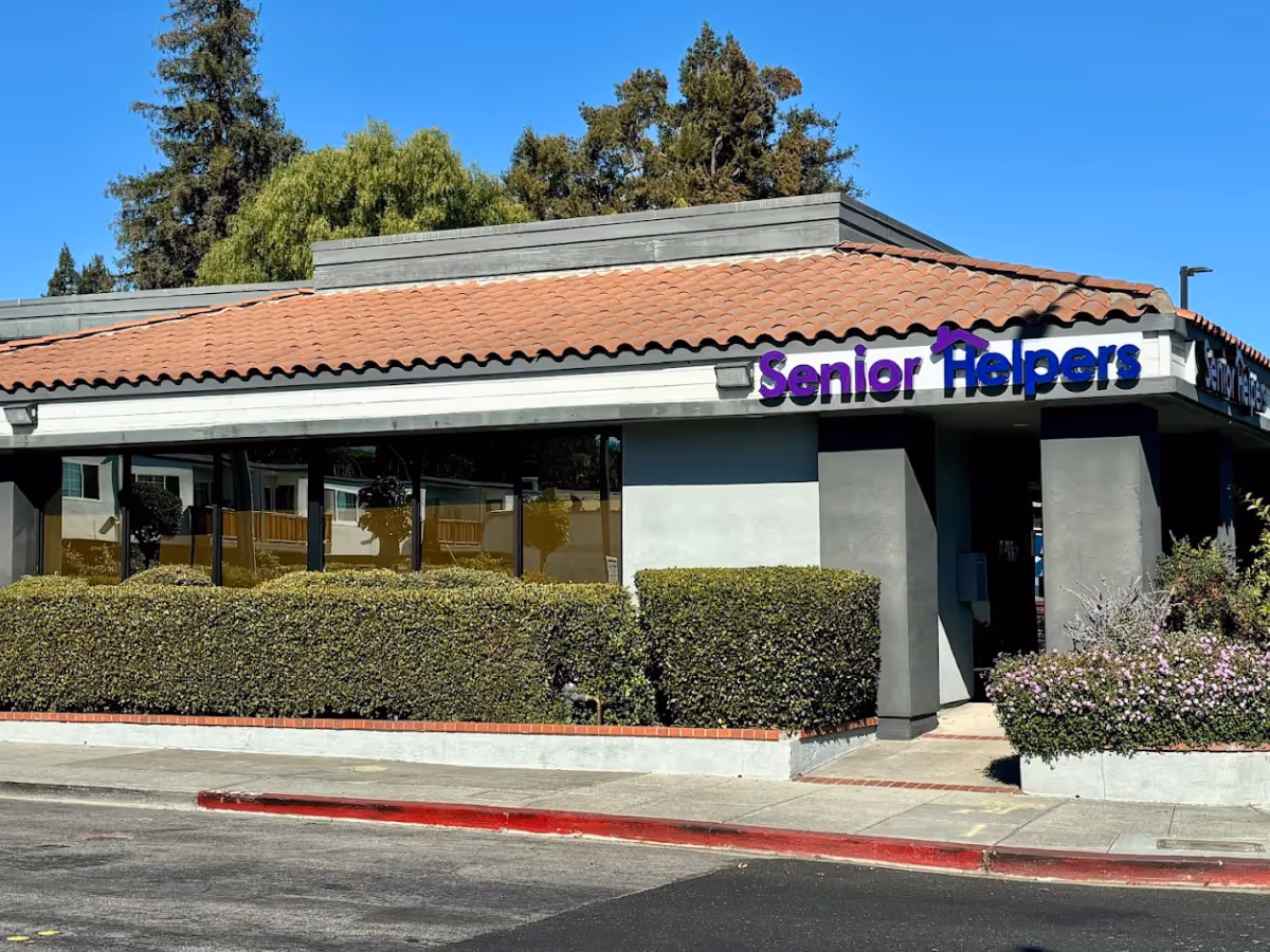 Exterior view of a Senior Helpers building with glass windows, hedges, and a tiled roof.