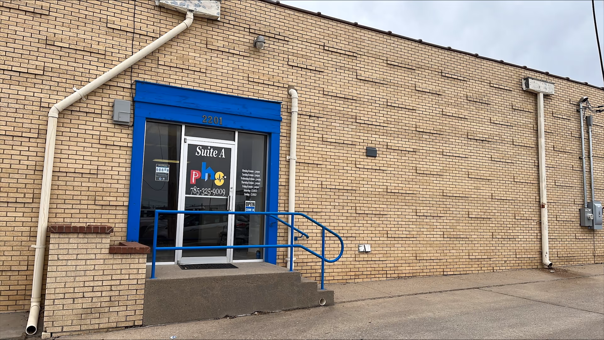 Brick building exterior with a blue-framed glass entrance, stairs and ramp labeled Suite A.