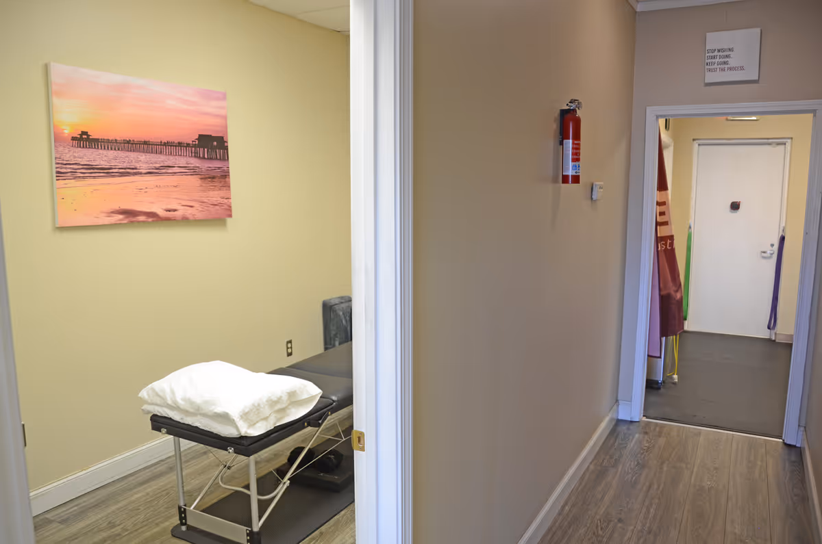 Narrow hallway with a treatment table and a framed sunset painting on the left wall.
