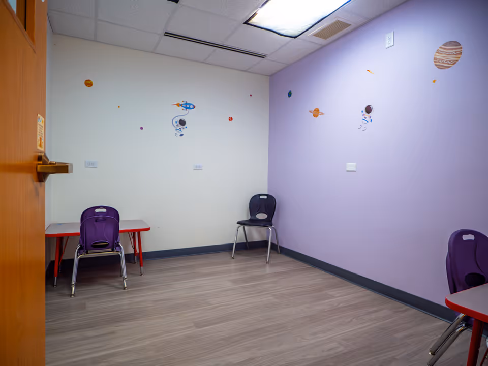 Interior activity room with pastel purple walls, space decals, and small tables with purple chairs.
