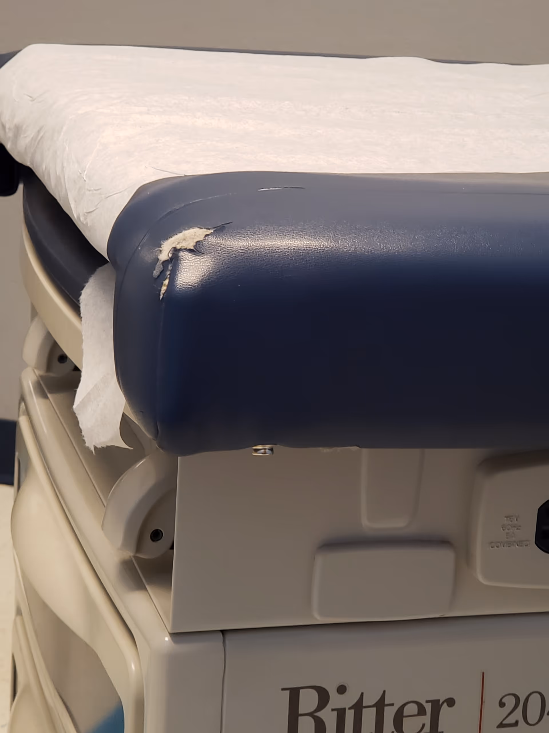 Close-up of a torn blue medical examination chair in a clinical setting.