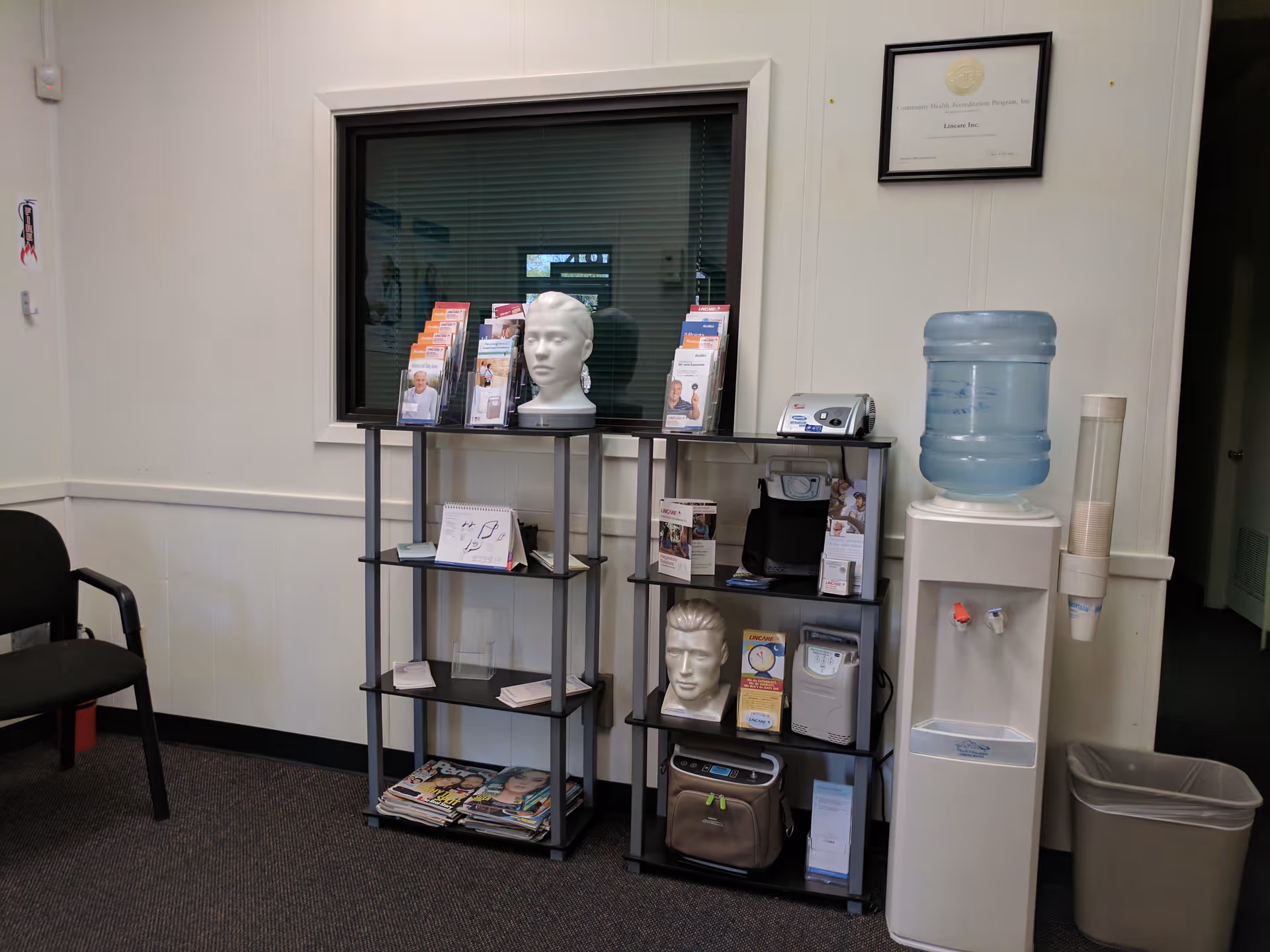 Indoor facility lobby with pamphlet racks, mannequin head, water cooler, and certificate on wall.