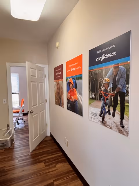 Interior hallway of a senior care facility with wall posters and an open door.