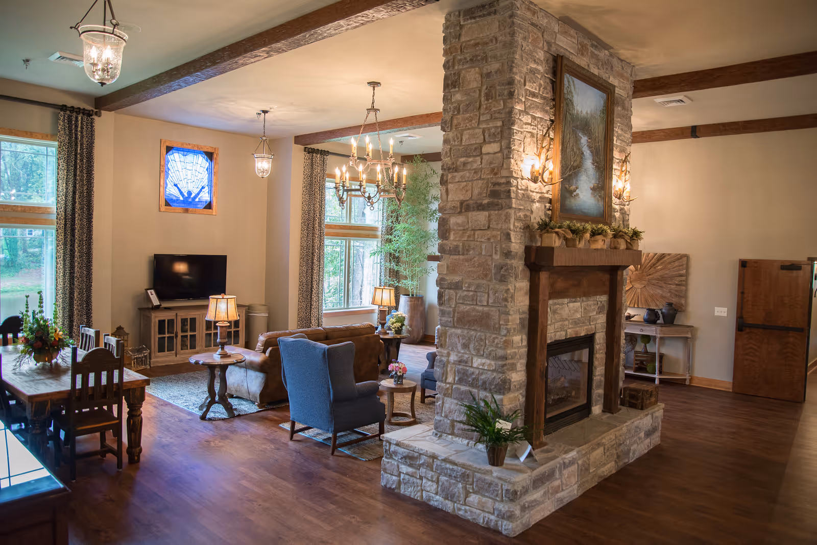 Open living area with stone fireplace, seating, dining table, and windows.