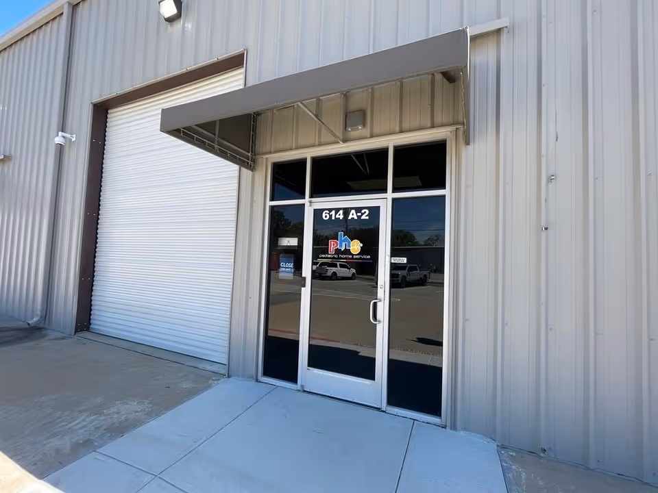 Exterior entrance of a metal building with glass doors and a logo reading Pediatric Home Service.