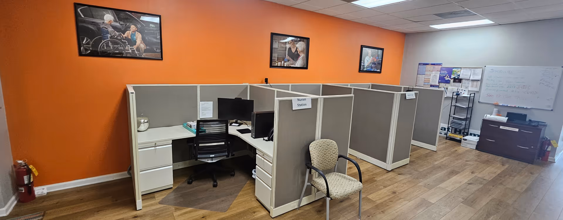 Panoramic view of an orange-walled nursing station with cubicles in a senior living facility.