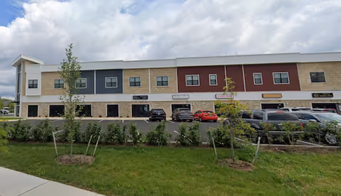 Exterior view of a strip mall-style building with multiple storefronts and parked cars.