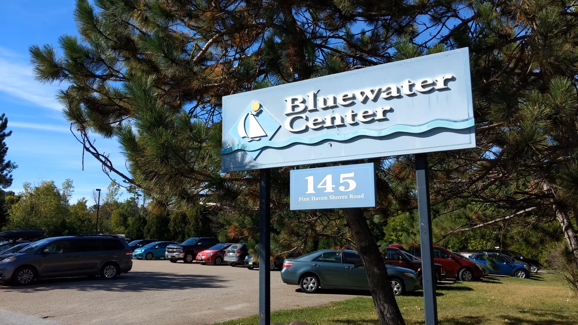 Outdoor parking lot with a Bluewater Center sign, trees, and parked cars.