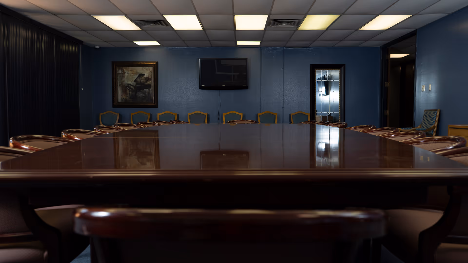 A long, polished conference table surrounded by wooden chairs in a blue-walled meeting room.