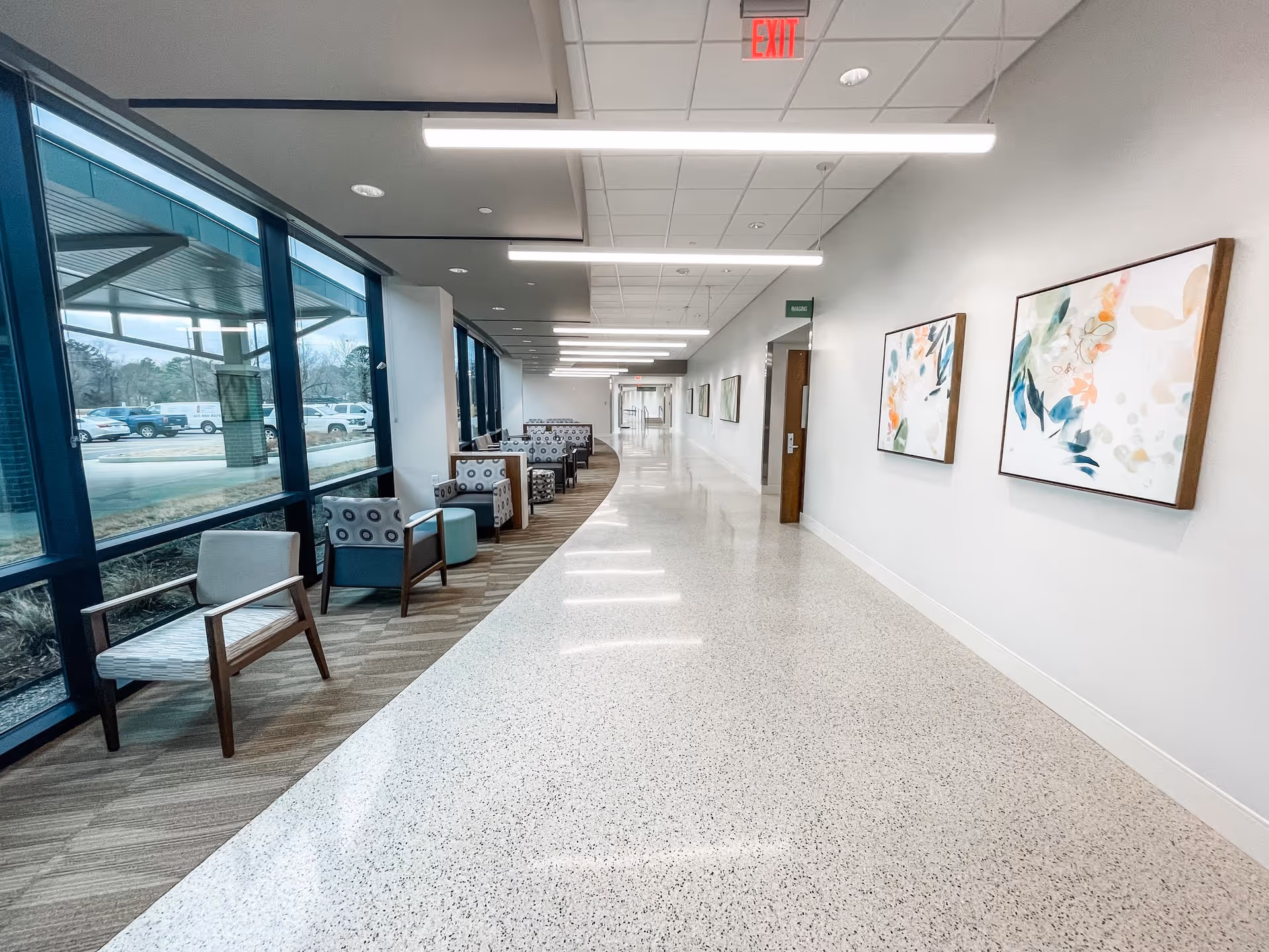 Bright, long interior hallway with window seating, modern art on walls, and overhead fluorescent lighting.