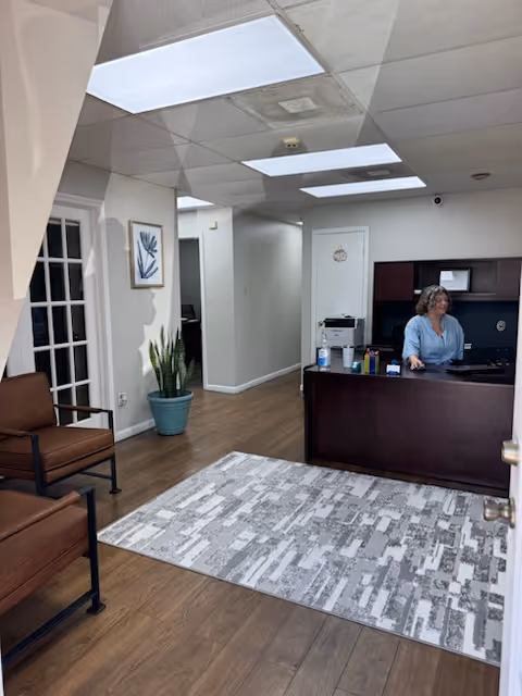 Reception area of a senior living facility with a front desk and a seated woman.
