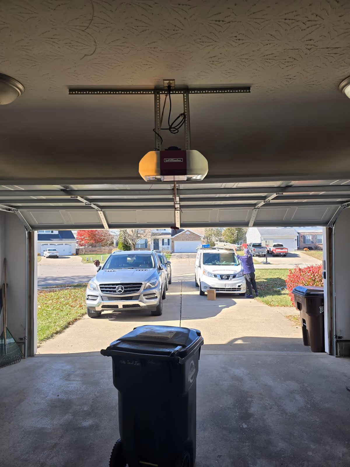 Garage interior with open door, driveway view of parked cars and a person outside.