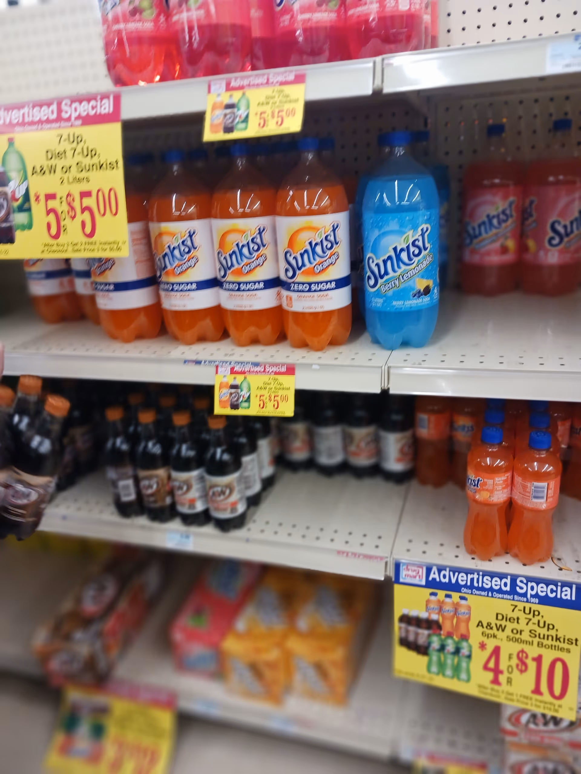 Rows of bottled drinks on store shelves with sale signs inside Discount Drug Mart.