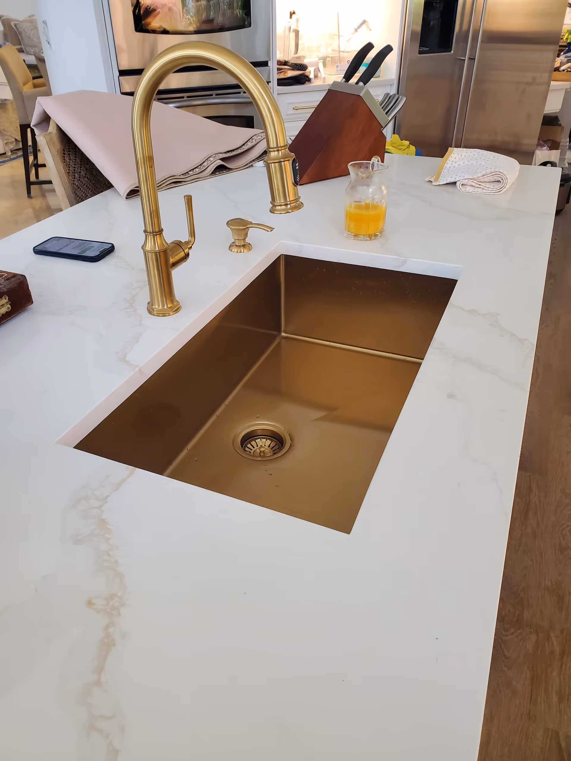 Gold faucet over a white marble island sink in a modern kitchen.