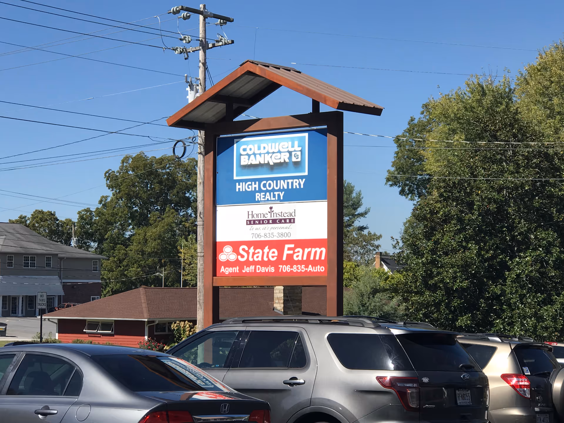 Freestanding sign structure in a parking lot displaying Home Instead, Coldwell Banker, and State Farm.