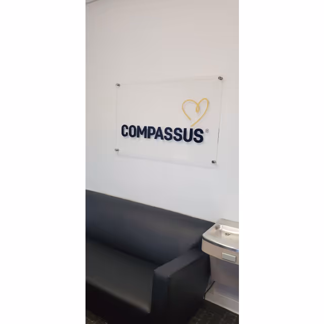 Interior lobby area with Compassus sign on wall and black sofa.
