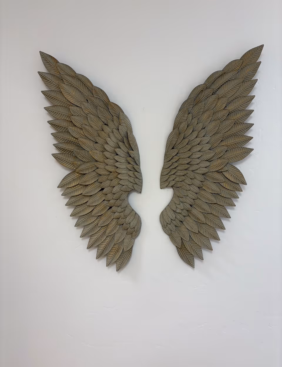 Two metallic wing sculptures mounted on a white interior wall.